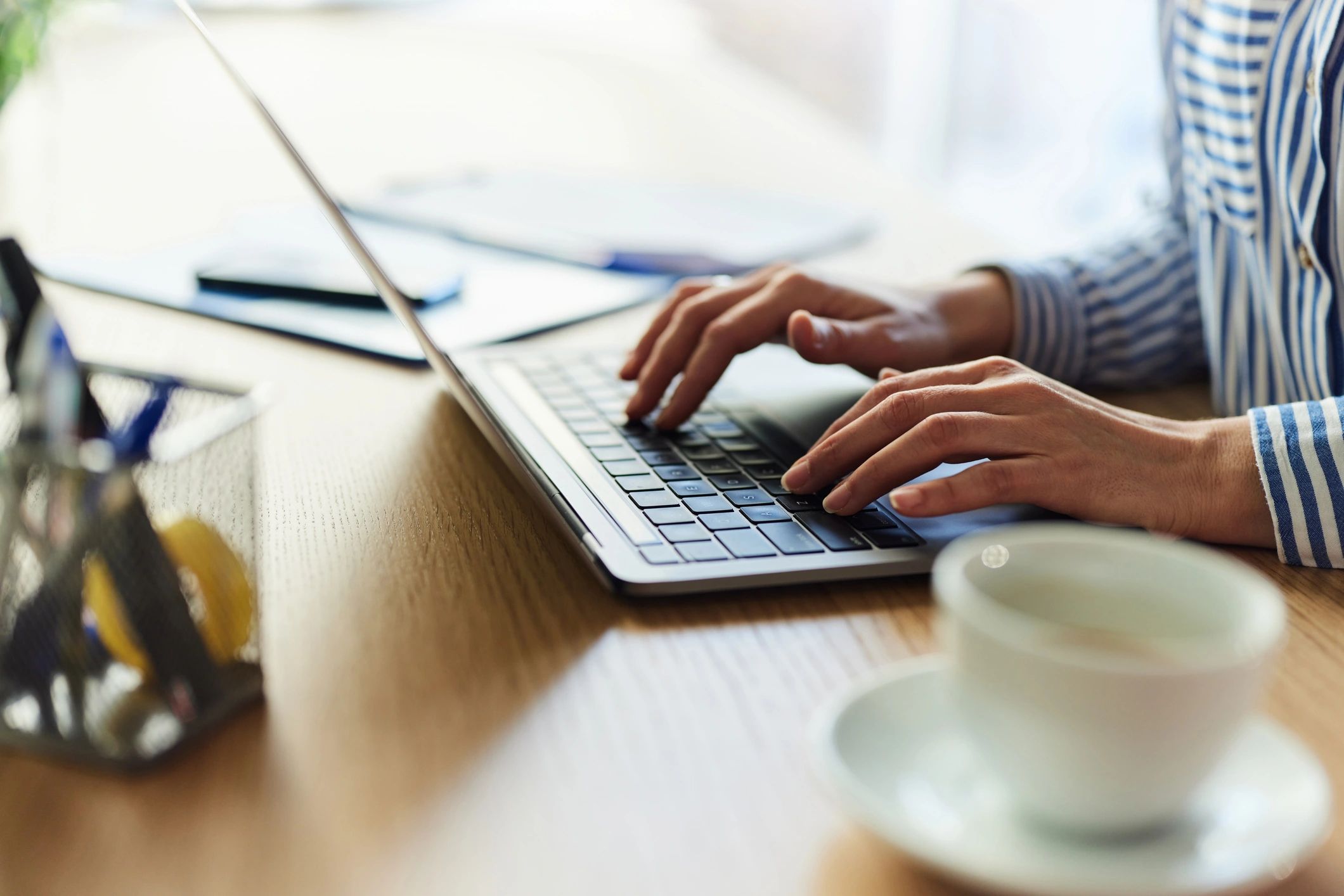 Person typing on a laptop at a desk with a coffee cup nearby.